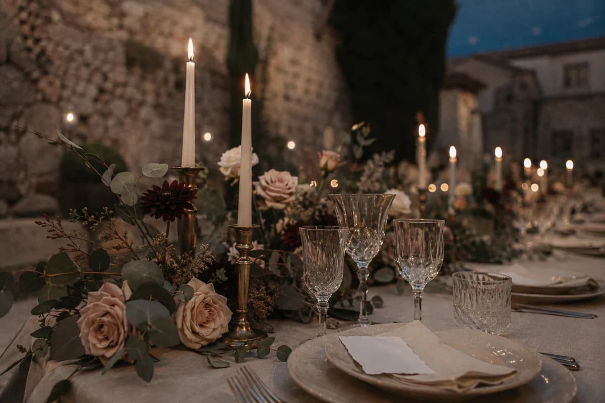 Mesa de boda en un patio de piedra, con velas, flores y pequeños detalles de papelería